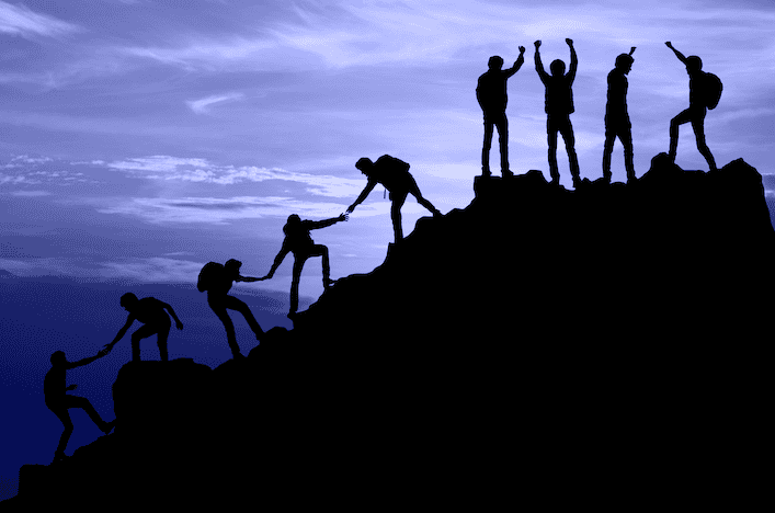 Nine individuals hiking to the top of a summit, some reaching back to help one another and some at the summit, raising arms in the air for achievement