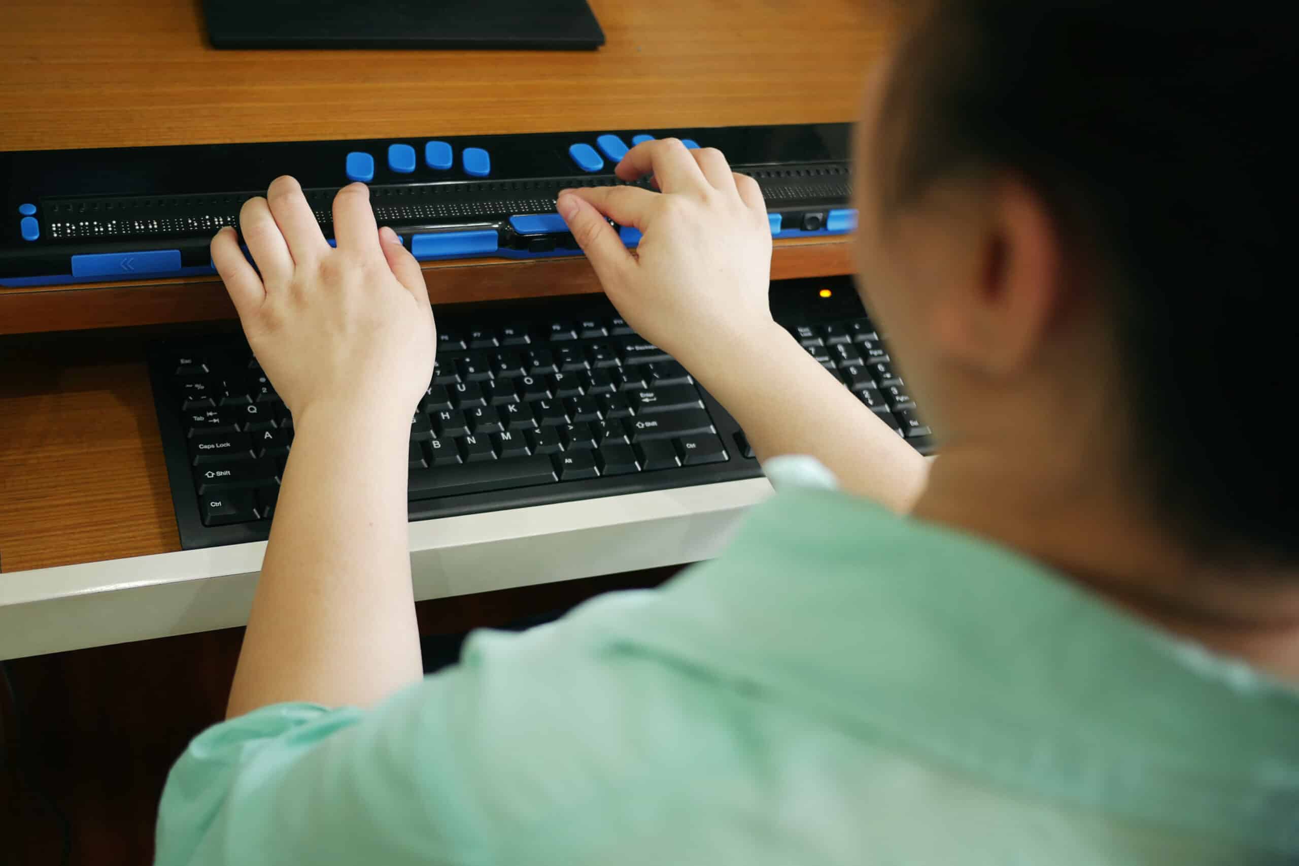 Rear view of person with blindness disability using computer keyboard and braille display or braille terminal a technology assistive device for persons with visual impairment