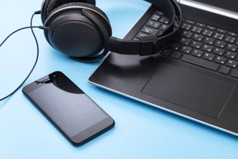 Close-up of a smartphone, over-ear headphones, and a laptop on a bright blue background to represent a screen reader