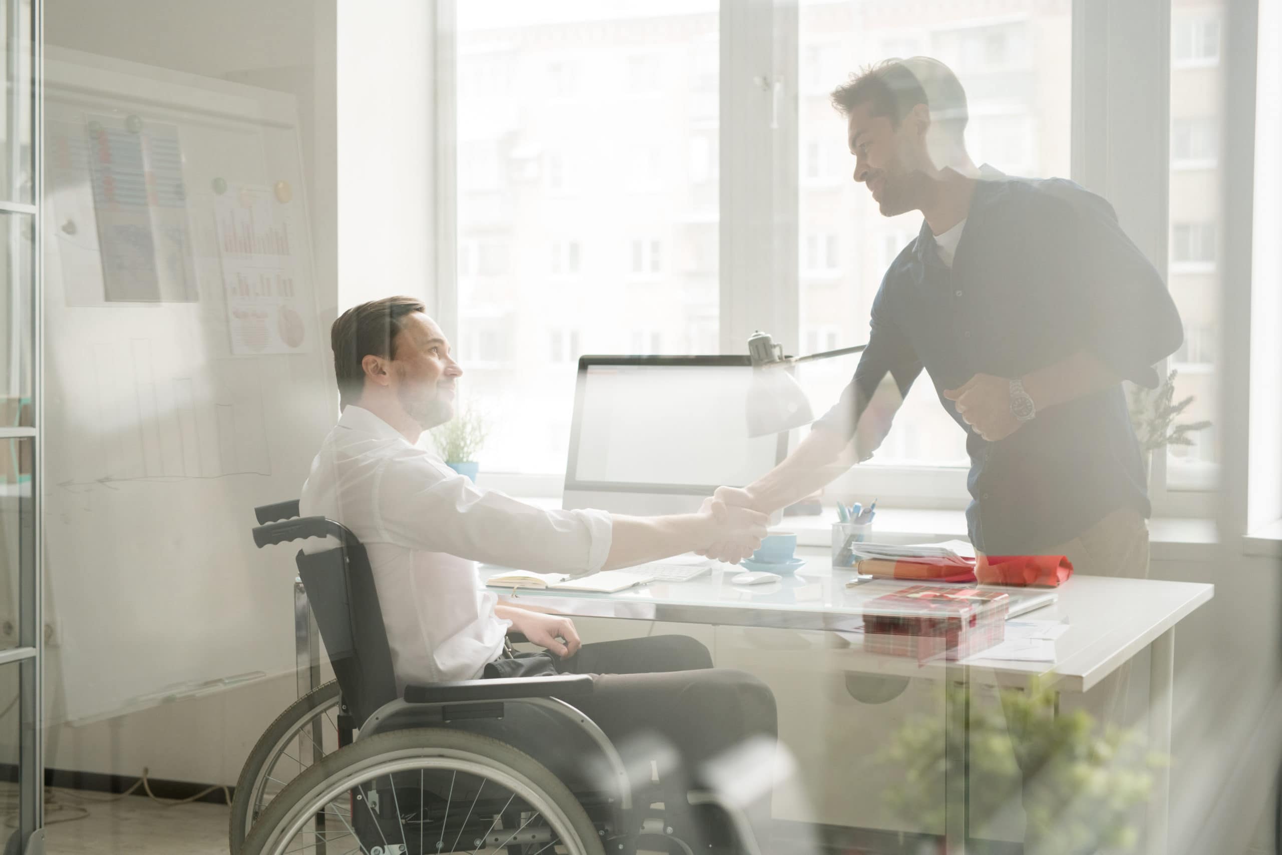 Businessman shaking hands with man in wheelchair behind the window at office